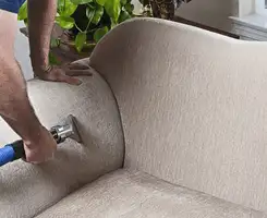 Professional upholstery cleaner deep-cleaning a fabric sofa with a handheld extraction tool and hose in {city}, {state}.